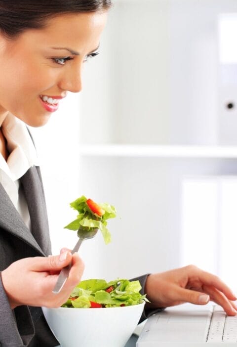 business woman eating salad on her desk while working on laptop