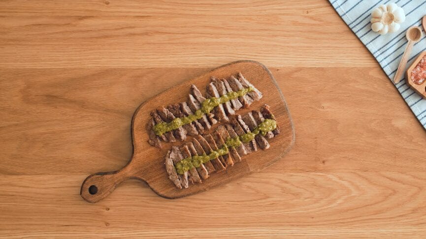 sliced pan-seared steaks with pesto sauce on a cutting board